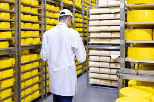 Trabajador en un almacen rodeado de estanterías llenas de quesos embalados